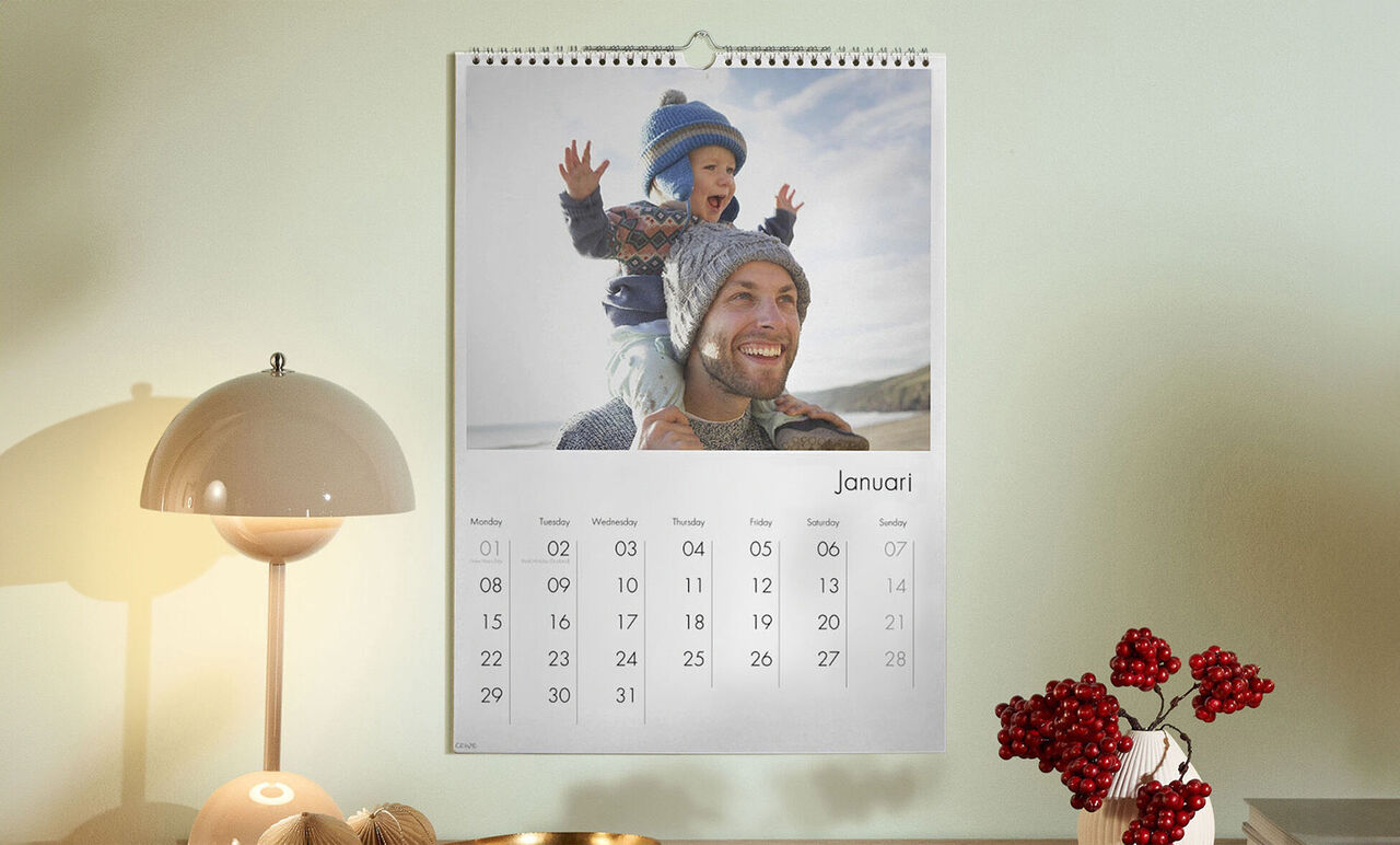 Een stijlvol opgehangen kalender toont een vrolijke januari met een kind in winterkleding zittend op een volwassene.