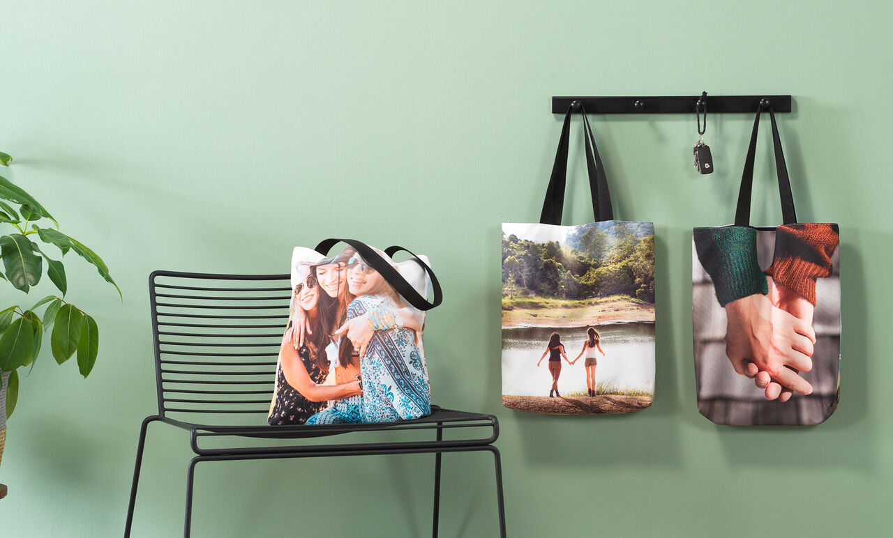 Drie creatieve tassen met foto's hangen aan een rek. Eén toont vriendinnen, een ander een landschap, de derde hand-in-hand paren.