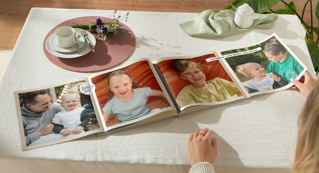 Iemand bladert door een CEWE-fotoboek op een tafel met een kopje en een bloemenarrangement.