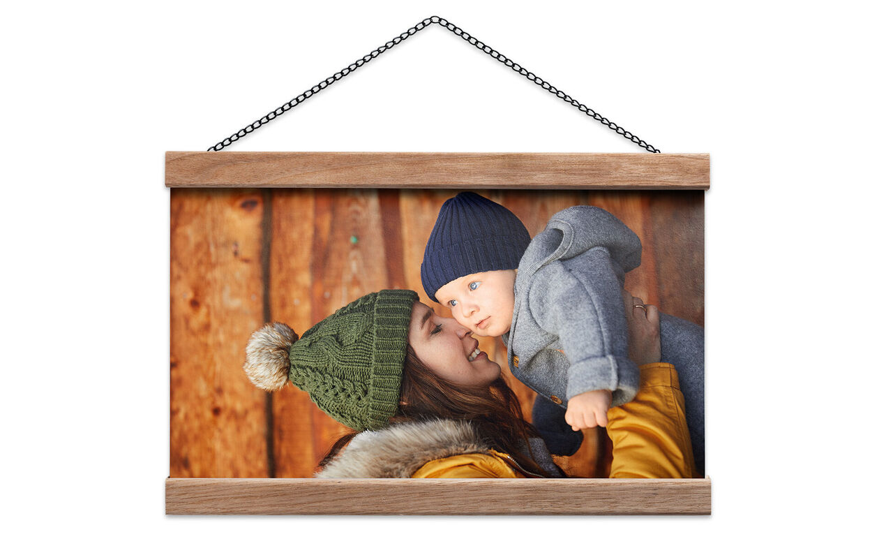Een lachende moeder houdt haar baby in warme kleding voor een houten muur.