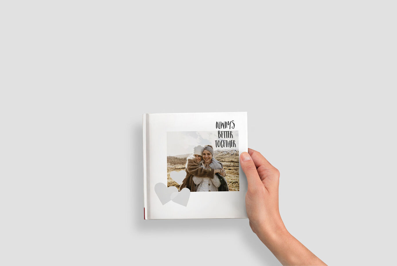 Een hand houdt een gepersonaliseerd fotoboek vast met de titel 'Always Better Together'. Het toont twee gelukkige mensen.
