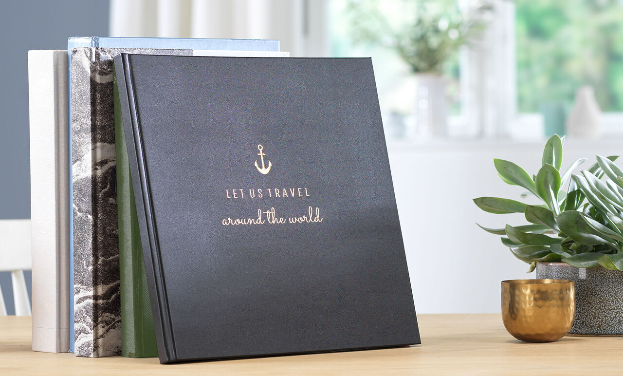 Zwart fotoboek met de titel 'Let Us Travel around the World' op een tafel.