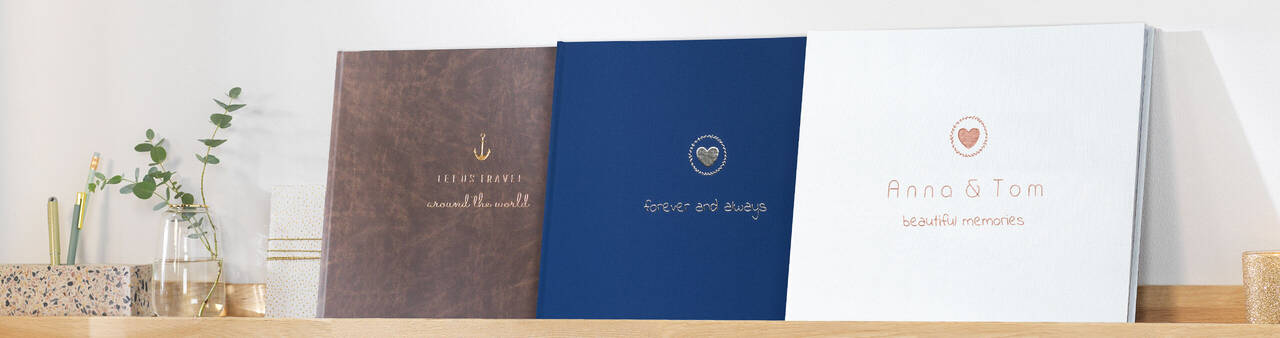 Drie prachtige CEWE fotoboeken op een plank. Ontwerpen in bruin, blauw en wit.
