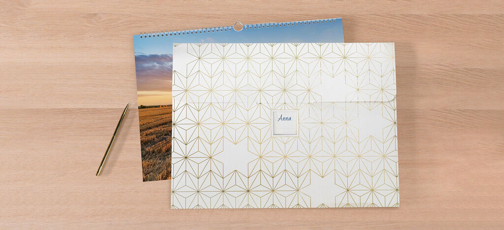 Elegante CEWE wenskaarten liggen met een kalender op tafel. Een gouden pen ligt ernaast.