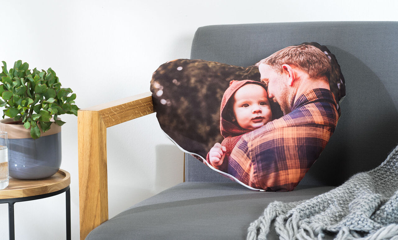 Een hartvormig kussen met een liefdevolle foto van een man en kind buiten.