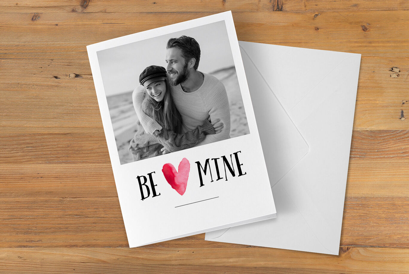 Een lachend paar omarmt elkaar voor een lichte achtergrond. Op de kaart staat 'BE MINE' in grote letters.