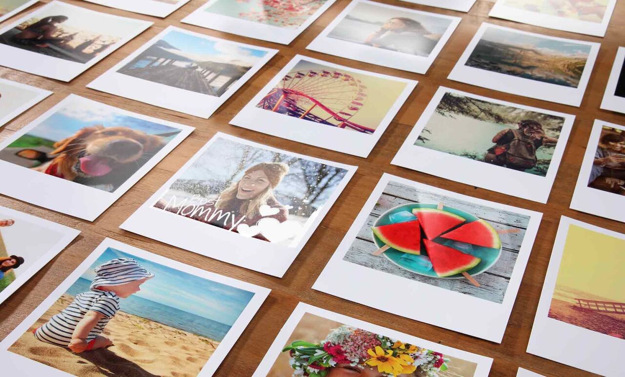 Allerlei fotoprints op een houten tafel. De foto's tonen gelukkige mensen, reisjes en kleurrijk fruit.