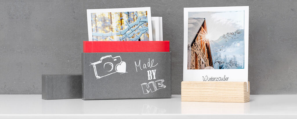 Zwarte doos met foto's op een witte tafel, grijze muur op de achtergrond.