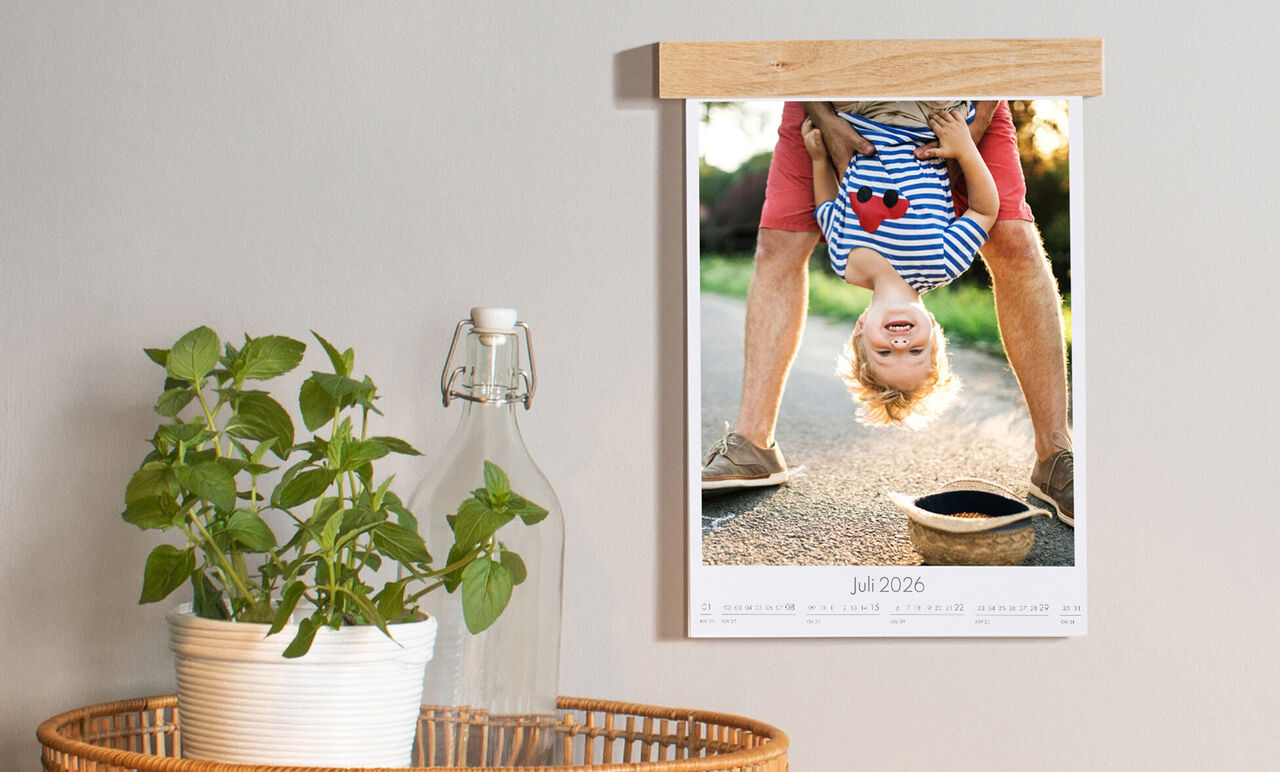 Een jongen op zijn kop in een wandkalender gehouden door een volwassene met zonnige straat op de achtergrond.