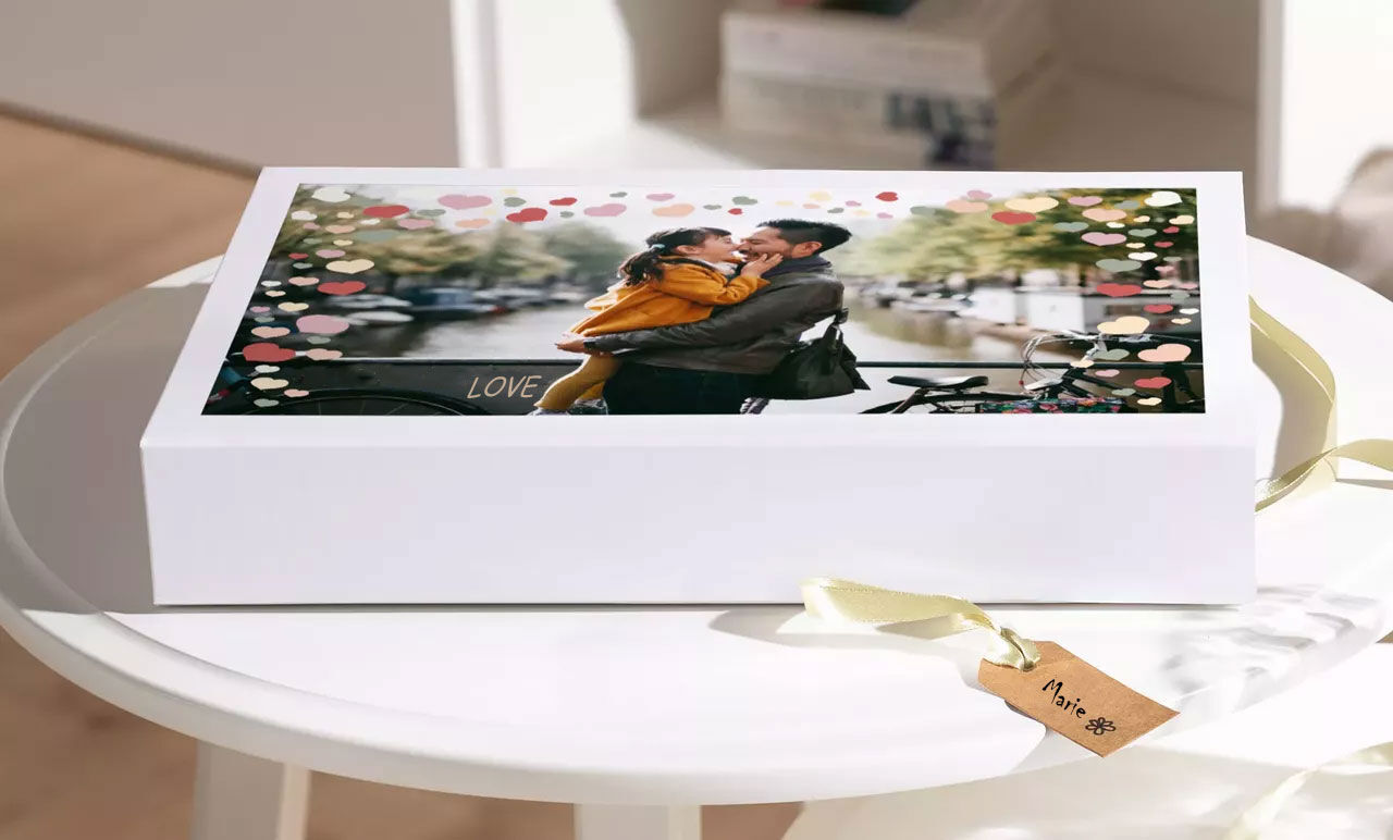 Een verliefd koppel omhelst elkaar aan een tafel met een cadeaudoos op de voorgrond.