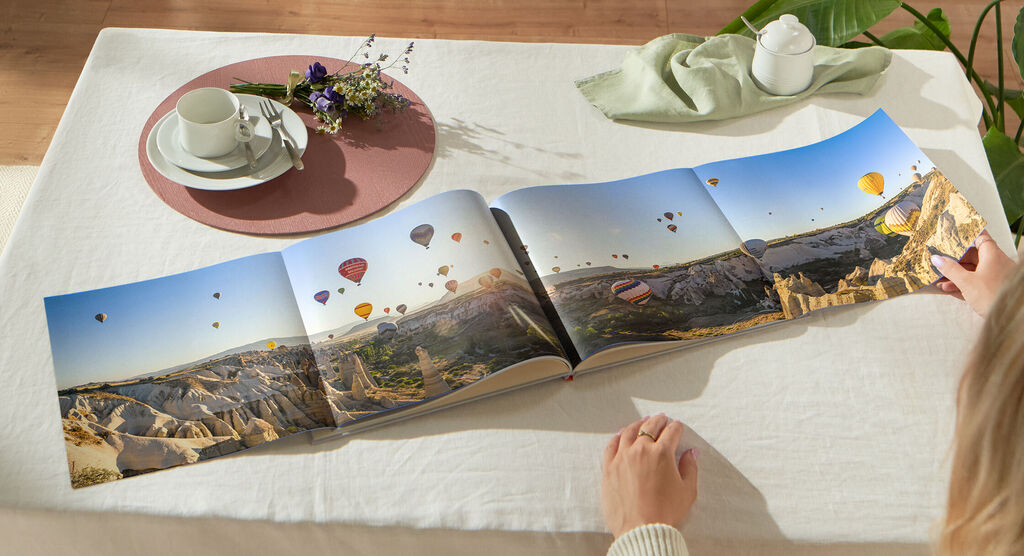 Iemand bladert door een open fotoboek met ballonnen en landschappen op de achtergrond.